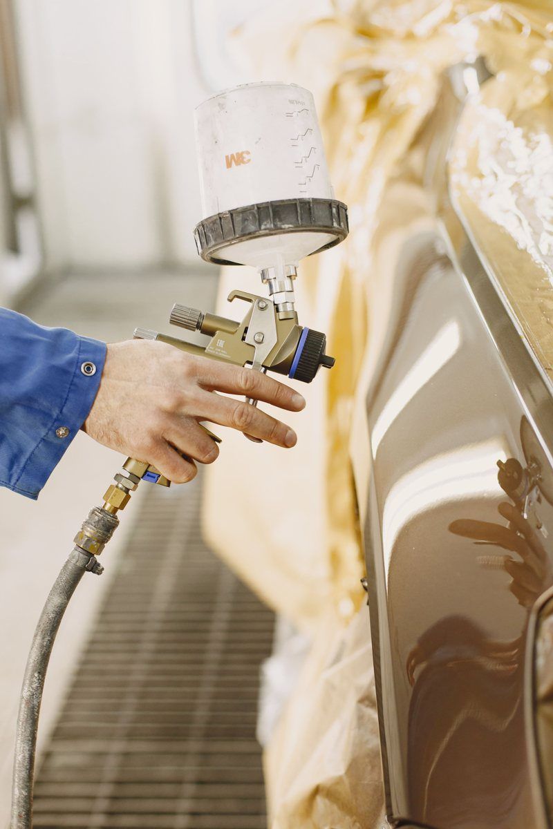 Automotive painter spraying paint onto a vehicle body panel in a professional paint booth